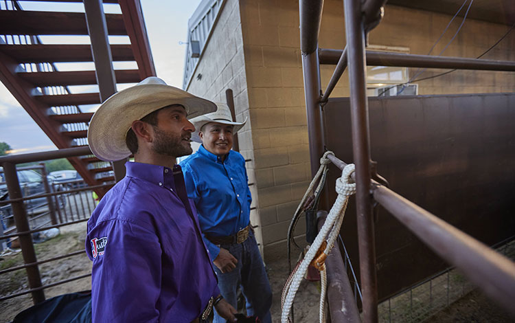 Dustin Boquet wearing a purple shirt and a hat talking with a friend wearing a blue shirt before the rodeo.